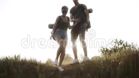 年轻夫妇带着背包徒步旅行男人支持女人而她下山太阳照耀着视频的预览图