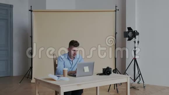 专业的男性帅哥摄影师在自己的摄影棚里用笔记本电脑工作他坐着修饰照片视频的预览图
