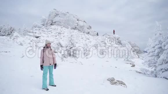 一个穿暖和运动衣的女孩站在白雪皑皑的山上下面视频的预览图