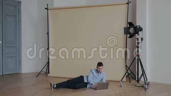 年轻英俊的男性视频记录器与笔记本电脑在舒适的位置工作而躺在地板上他把视频剪辑成视频的预览图