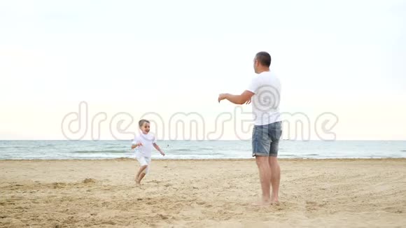 一个快乐的小男孩沿着沙滩跑去见他的父亲快乐的爸爸把孩子抱在怀里亲吻他视频的预览图