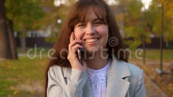 年轻漂亮的女人在公园里用手机说话女孩微笑漂亮的女商人手里拿着一个视频的预览图
