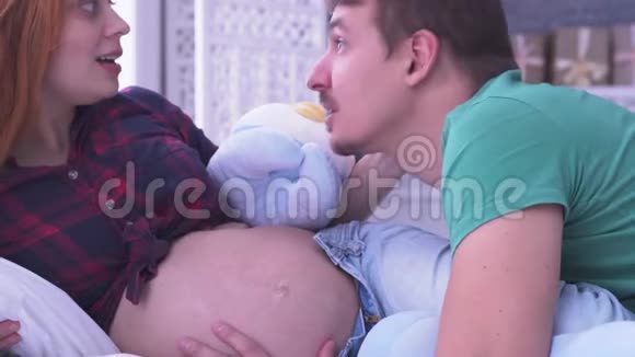 孕妇和丈夫躺在床上男人亲吻妻子的腹部怀孕视频的预览图