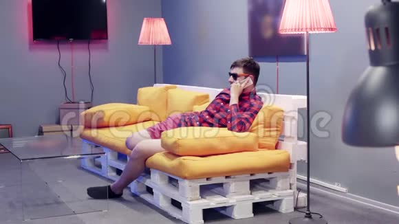 可爱的家伙戴着太阳镜坐在橙色沙发上在现代房间里打电话视频的预览图