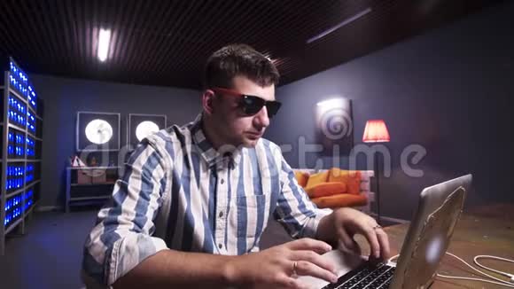 一个留着胡子戴着太阳镜的人坐在办公桌后面在灰色笔记本电脑上打字视频的预览图