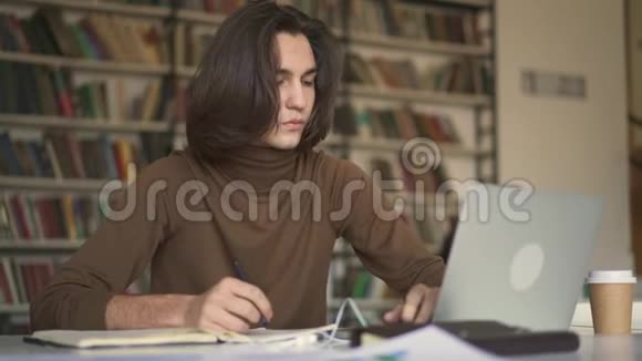 坐在图书馆里的一个长发青年在翻笔记本视频的预览图