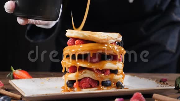 烹饪艺术厨师把焦糖铺在一堆用森林浆果装饰的新鲜蓬松煎饼上自制视频的预览图