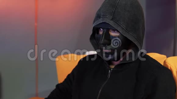 有人戴着黑色的面罩和深灰色的帽衫坐在橙色的沙发上视频的预览图