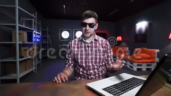 有趣的留胡子的家伙坐在桌子后面在黑暗的房间里拿着笔记本电脑视频的预览图