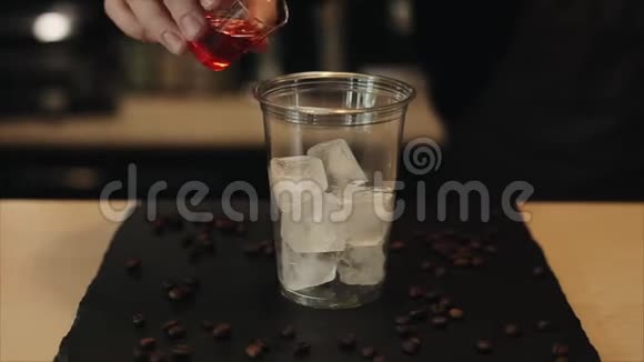 咖啡师将草莓糖浆柠檬水和浓缩咖啡倒入一个装有冰块的杯子中特写视频的预览图