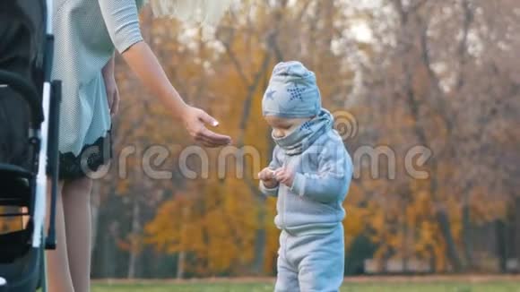 年轻的妈妈带着一个婴儿在秋天的公园里散步妈妈把垃圾从孩子手拿走视频的预览图