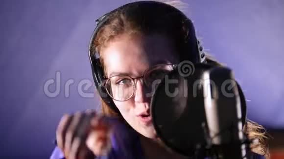 一位戴着耳机在摄影棚里唱着歌的情绪激动的年轻女子看着镜头视频的预览图