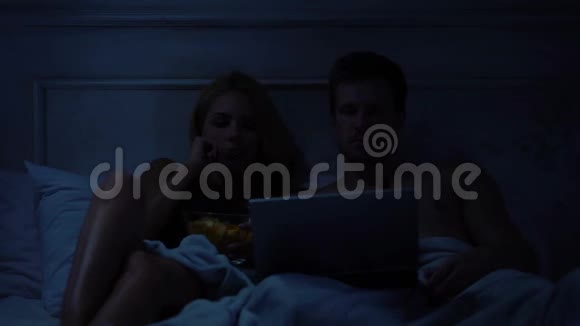 一对夫妇在笔记本电脑上看心理惊悚片吃零食看恐怖电影视频的预览图