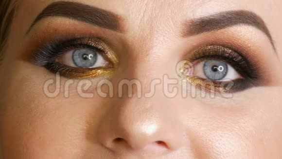 美丽的胖女模特金色的妆容烟熏的眼睛深红色的口红假睫毛蓝色的眼睛摆在黑色的脸上视频的预览图