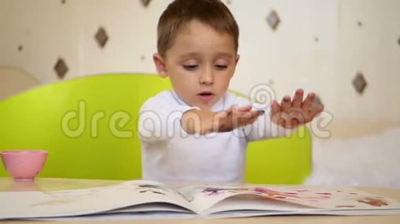 快乐学龄前儿童从事绘画一个淘气的男孩拿着油漆拍着他的手掌在纸上视频的预览图