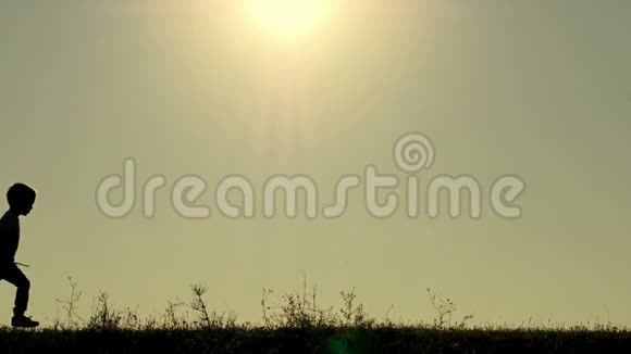 日落时分一个快乐的孩子在草地上奔跑的剪影走游戏旅程视频的预览图