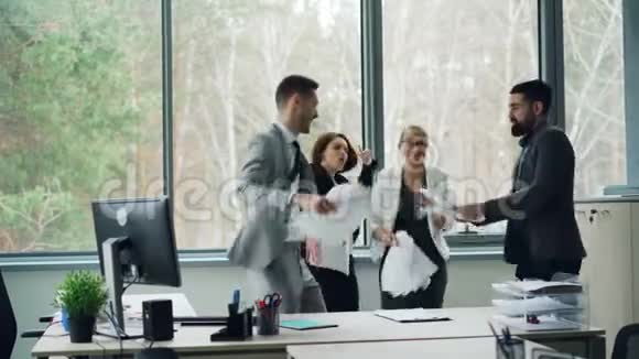 快乐的男人和女人在办公室里举行聚会用纸跳舞然后把它们扔到空中笑青年视频的预览图