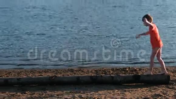 穿着红色t恤的男孩在河岸海滩上的一根木头上视频的预览图
