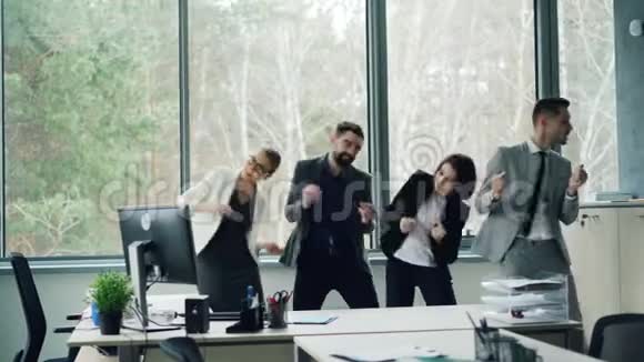 年轻同事的欢乐团队穿着西装在现代办公室跳舞他们的手臂和身体都在微笑和欢笑视频的预览图