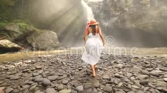 穿着白色连衣裙和草帽的年轻女孩跑到特根甘瀑布和举起手臂免费生活旅行4K视频的预览图