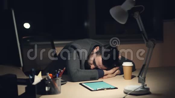 一个穿西装的疲惫的家伙在忙碌的工作日后深夜睡在办公室的办公桌上打开电脑外卖视频的预览图