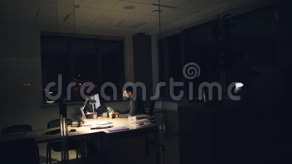 穿西装打领带的疲倦商人在办公室里用电脑工作晚上坐在黑暗的房间里的工作台上视频的预览图