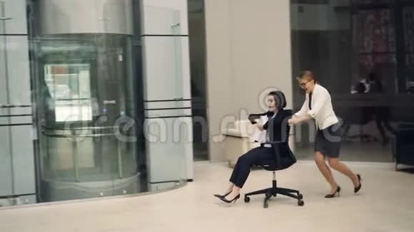 女商人们在办公室大厅里玩得很开心坐着椅子扔着文件享受自由和休息视频的预览图