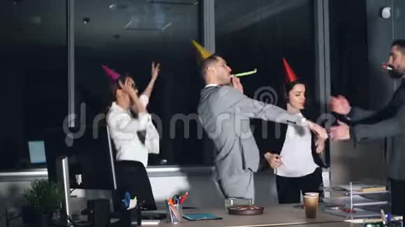快乐的年轻人在公司聚会上跳舞戴着派对帽吹着喇叭生日蛋糕和生日蛋糕视频的预览图