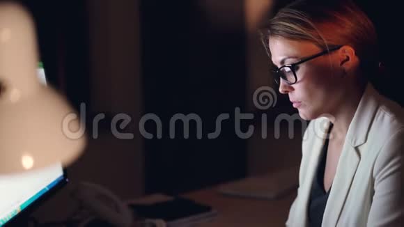 一个年轻漂亮的商务女性在深夜用电脑打字坐在办公桌前用键盘打字视频的预览图
