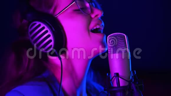 情绪化的年轻女子戴着耳机在工作室唱歌紫色霓虹灯照明视频的预览图
