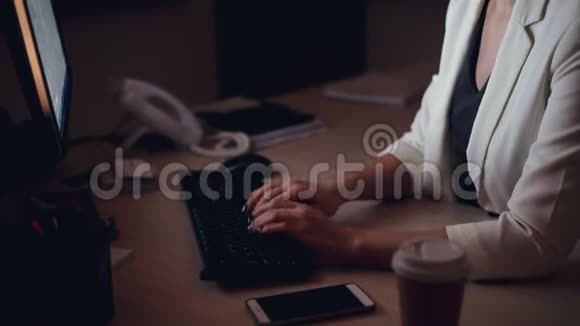 一张严肃的年轻女人在电脑打字看着屏幕独自坐在黑暗的工作台上的倾斜镜头视频的预览图