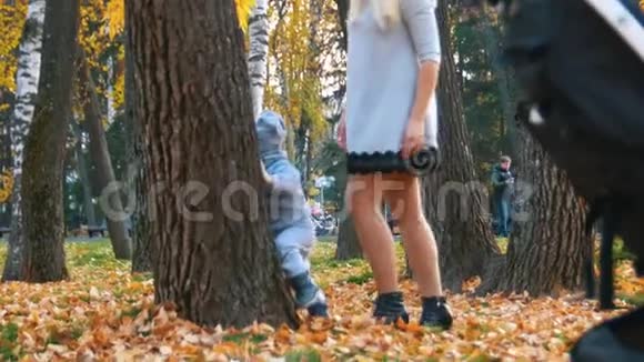 年轻的妈妈穿着裙子和她的小宝宝在秋天公园玩捉迷藏幸福家庭视频的预览图