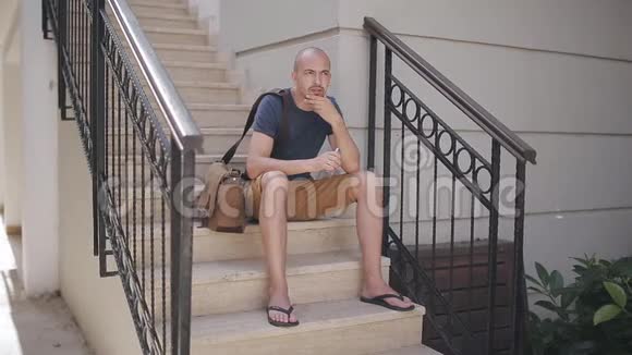 穿短裤的男人坐在楼梯上用智能手机等待顾客视频的预览图