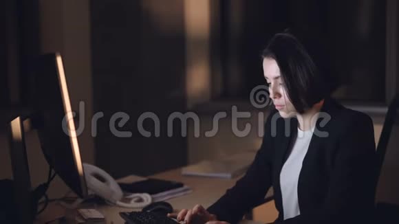 穿着正式西装的女商人正在上电脑夜班坐在办公桌前打字看屏幕忙碌的年轻人视频的预览图