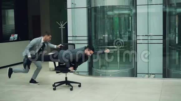 玩的商人们在办公室大厅里的骑椅上玩得很开心在摇椅上玩赛车游戏视频的预览图