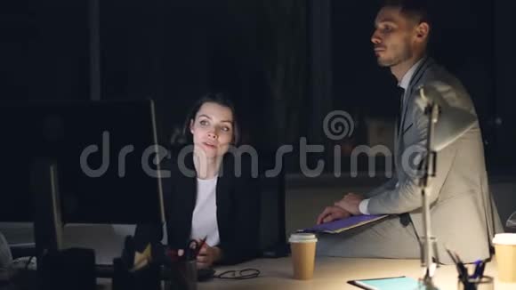 严肃的商人穿西装的男人和女人深夜在黑暗的办公室里工作看着电脑屏幕和电脑屏幕视频的预览图