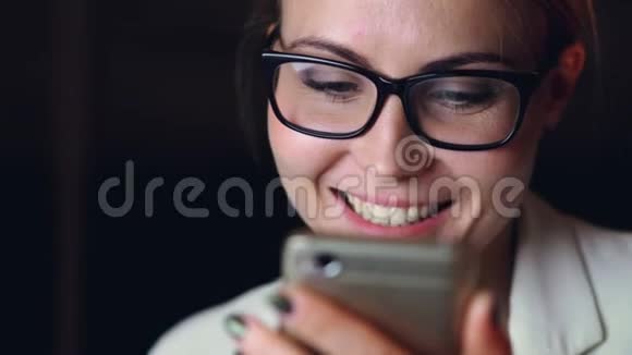 使用智能手机触摸屏幕和微笑享受交流的漂亮女孩戴眼镜的特写镜头视频的预览图