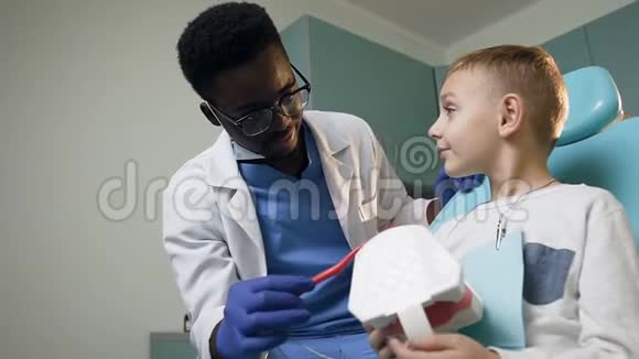 年轻的非洲牙医教小男孩如何使用牙刷使用塑料牙齿视频的预览图
