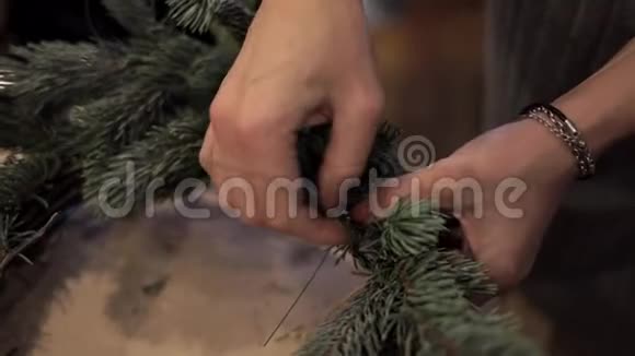 女性用一根绿色的铁丝把木棒捆紧做成圣诞花环视频的预览图