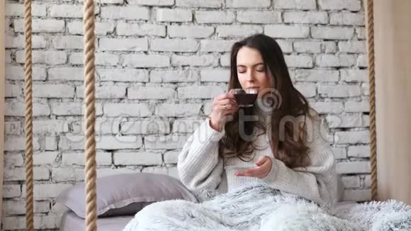 年轻漂亮的女人在家里的床上喝着香气扑鼻的咖啡视频的预览图