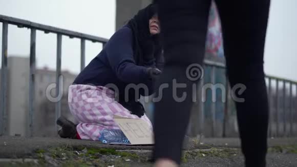 成年无家可归的妇女伸出手在寒冷多风的灰色天气中坐在桥上请求施舍和帮助视频的预览图