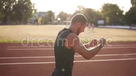 室外拍摄的年轻运动员男性伸展他的手在体育场的跑道上穿黑色T恤和衬衫的人太阳视频的预览图