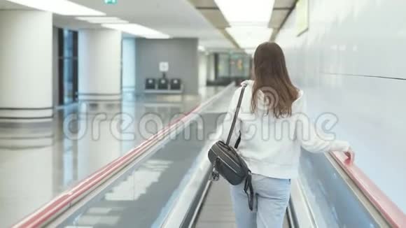 后景女士穿着运动服和背包在机场的移动走道上视频的预览图