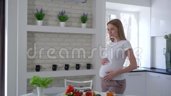 准女孩摸着她的大腹便便站在餐桌旁吃着鳄梨的水果和蔬菜视频的预览图