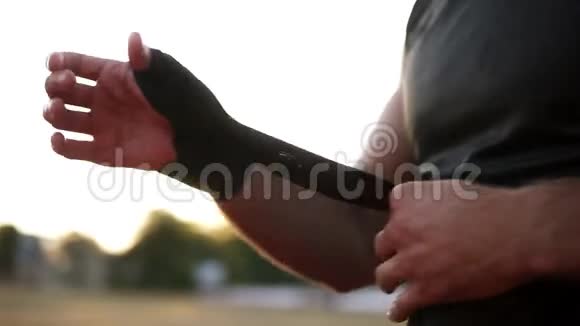 年轻的手包裹手用绷带在夏日户外锻炼穿黑色T恤的肌肉年轻拳击手视频的预览图