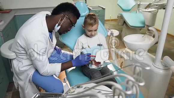 非洲男性牙医使用塑料牙齿模型教小男性病人如何使用牙刷视频的预览图