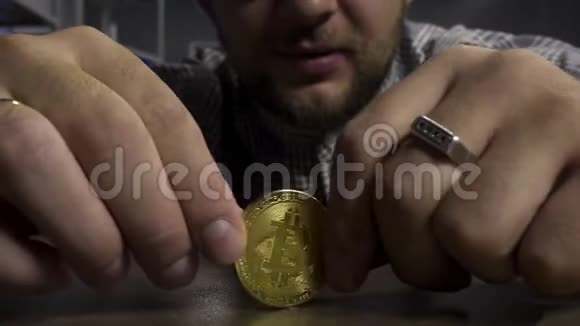 戴太阳镜的年轻人高兴地在棕色桌子上旋转着新的大金比特币硬币视频的预览图