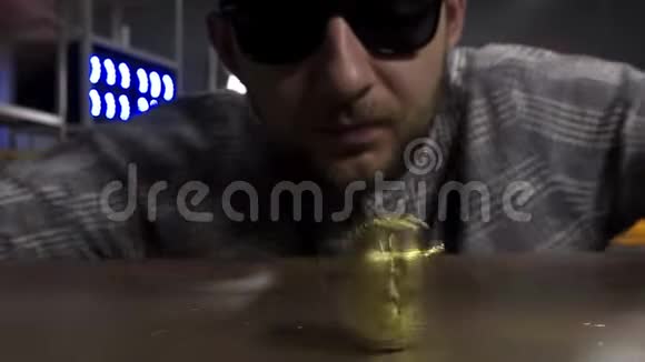 戴着太阳镜的可爱的年轻男性在棕色桌子上旋转着新的黄金比特币硬币视频的预览图