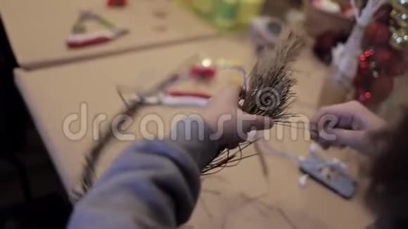 女用手在铁丝上编织花圈把干松枝缠在地上视频的预览图