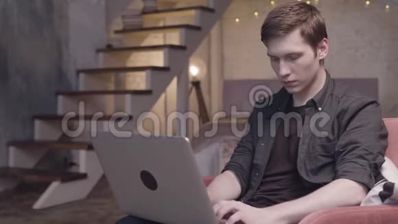 年轻男子与笔记本电脑在扶手椅在复式平面内部背景自由职业概念库存录像男性视频的预览图